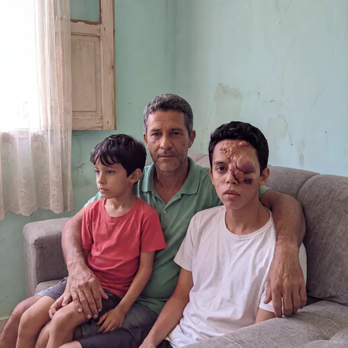 Murilo sentado no sofá de casa com o pai e o irmão mais novo