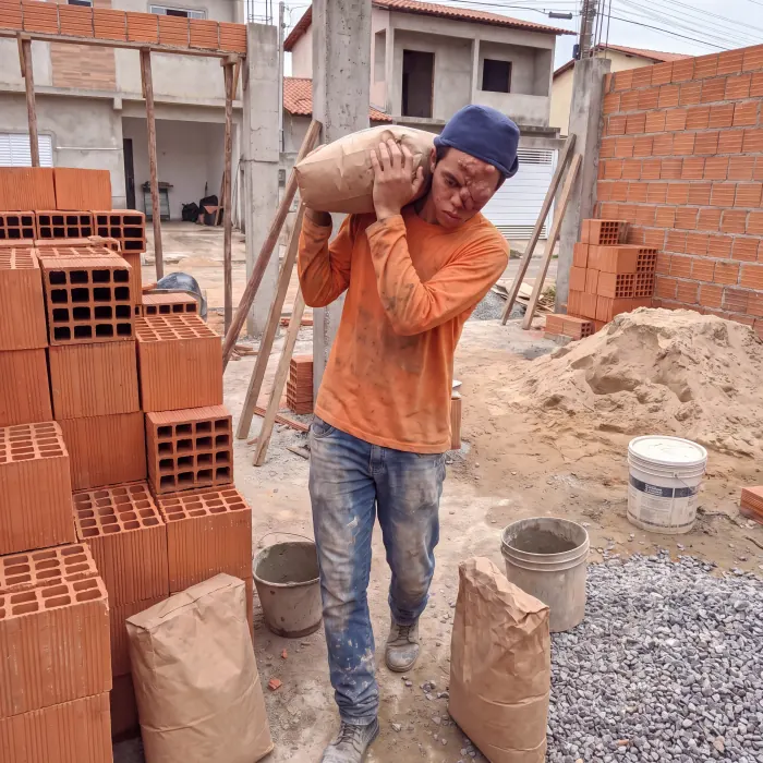 Murilo carregando um saco de cimento nas costas no canteiro de obras